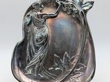 une assiette ancienne en argent sur laquelle est représentée une dame tenant un oiseau