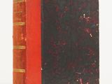 an old red and black book sitting on top of a white surface