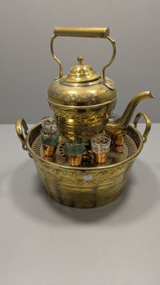 une théière en laiton avec des tasses à thé posées sur un plateau, le tout sur une table