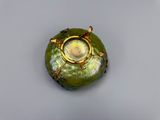 un vase vert bordé d'or posé sur une surface blanche