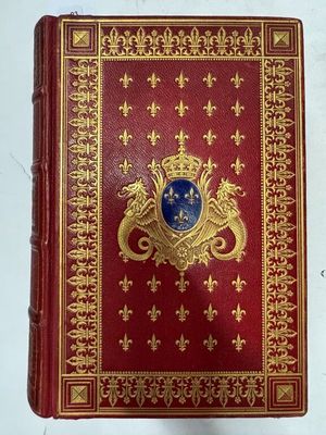un vieux livre rouge aux tranches dorées, orné d'un blason bleu sur la couverture