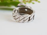 a close up of a silver ring on a table with a plant in the background