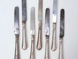 six silverplated knives are lined up on a white surface