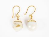 une paire de boucles d'oreilles composées d'une perle blanche montée sur un crochet plaqué or