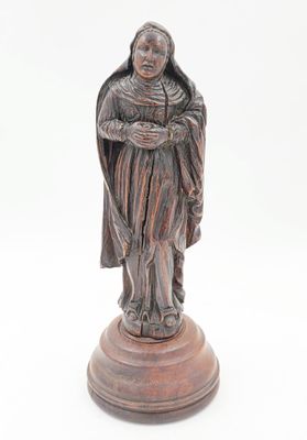 une vieille statue représentant une femme tenant un enfant dans ses bras, posée sur un socle en bois