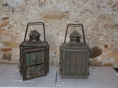 two metal lanterns sitting on a table in front of a brick wall