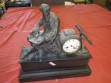 une statue représentant un homme assis sur une table, avec une horloge