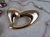 a gold heart shaped brooch on a table next to other jewelry