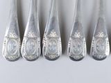 six silver spoons with ornate designs are lined up on a white surface