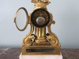 a gold clock on a marble base with a magnifying glass