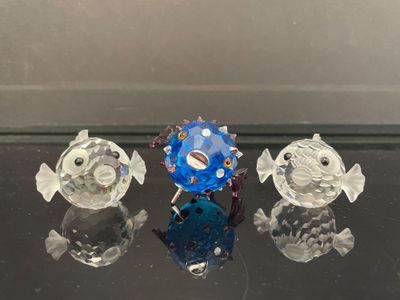 trois figurines de poissons en verre posées sur une table en verre