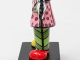 figurine of a woman in a pink coat with a red shoe on a black base