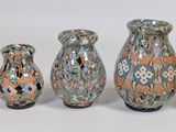 three vases with different designs are lined up on a white surface