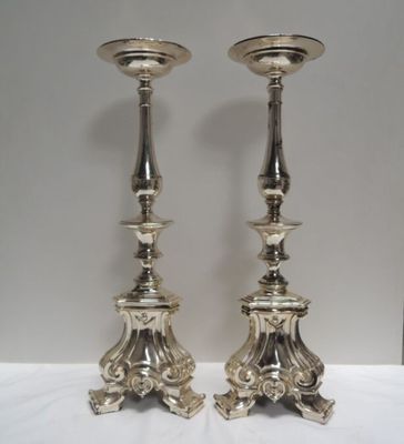 une paire de bougeoirs plaqués argent posés sur un socle, sur une table blanche