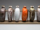cinq vases posés sur un socle en bois, sur un fond gris