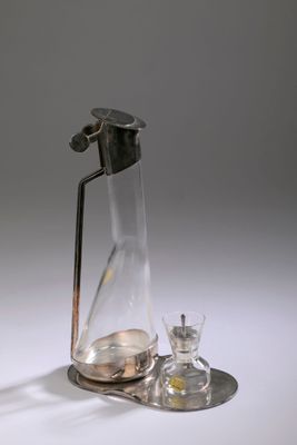 une carafe en verre munie d'une poignée en métal, à côté d'un verre