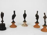 six figurines d'oiseaux en bronze posées sur des socles, disposées sur une surface blanche