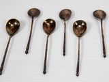 six cuillères anciennes sont alignées sur une surface blanche