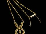 a gold necklace with green and white stones on a black background
