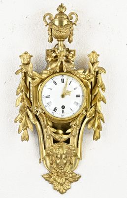 a gold clock hanging on the wall with a white wall behind it