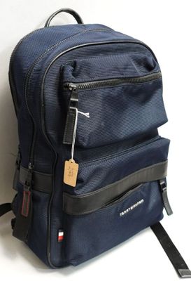 un sac à dos bleu muni d'une étiquette, posé contre un mur