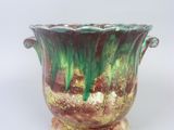 a green and brown vase sitting on a white surface