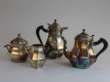 three silver teapots and two silver cups on a table