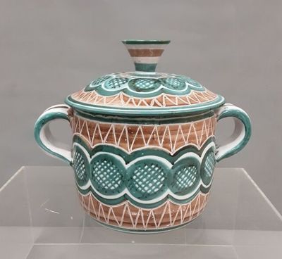a green and white pot with a lid on a clear shelf