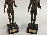 deux statues en bronze représentant un homme et une femme, posées sur des socles en marbre