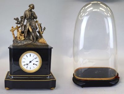 deux horloges posées sur une table, sous un dôme en verre