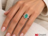 woman ' s hand with a diamond and emerald ring on her finger