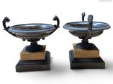 une paire d'urnes antiques en bronze posées sur des socles en marbre, sur fond blanc