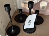 trois bougeoirs noirs posés sur une table, sur laquelle se trouve un mot
