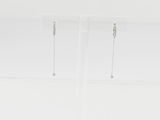 une paire de boucles d'oreilles en argent posée sur un socle en acrylique transparent, sur une surface blanche