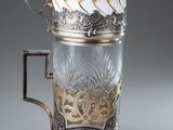 an antique silver and glass cup with a handle on a table