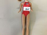 poupée Barbie portant un maillot de bain rouge avec une étiquette portant son nom