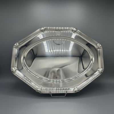 a silver plate with a handle on a gray surface