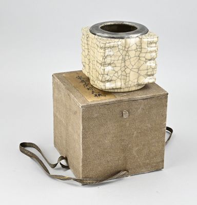 un vase beige et noir posé sur une boîte, sur une surface blanche