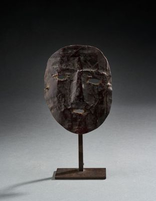 un masque en bronze posé sur un socle en bois, sur fond noir