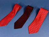 three ties are lined up on a blue surface, one red and one black