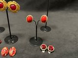 several pairs of red and gold earrings are displayed on a black surface