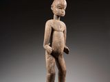 une statue en bois représentant un homme debout sur un socle noir