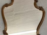 un miroir à cadre doré accroché à un mur blanc, avec un mur de briques en arrière-plan