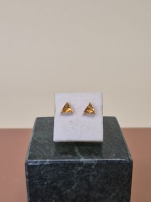 boucles d'oreilles en forme de triangle doré posées sur un bloc de marbre