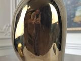 a silver vase sitting on a wooden table with a painting in the background