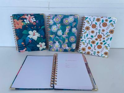 trois cahiers alignés sur une table, ornés d'un motif floral