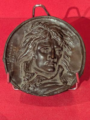 une image représentant un médaillon en bronze orné du visage d'un homme