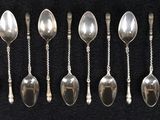 six cuillères en argent sont disposées en rangée sur une surface noire