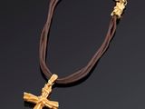 une croix en or suspendue à un cordon marron et à une chaîne en or