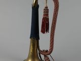 une vieille cloche en laiton à laquelle est suspendu, au niveau du col, un pompon rouge et bleu